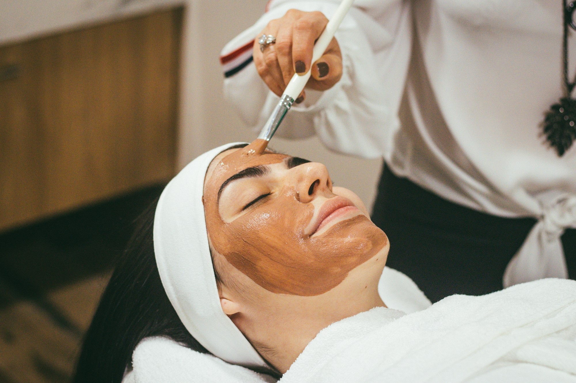 A therapist brushing a golden treatment mask across a guest's face in candlelight